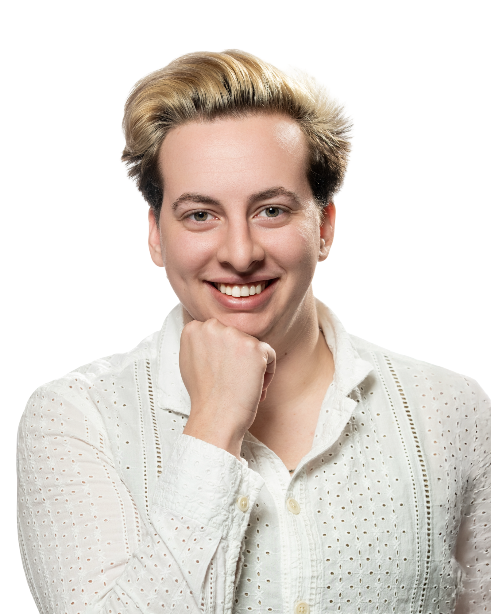A man with short, two-tone blonde and dark hair, smiling, resting his chin on his hand, wearing a white, eyelet-patterned shirt against a white background.
